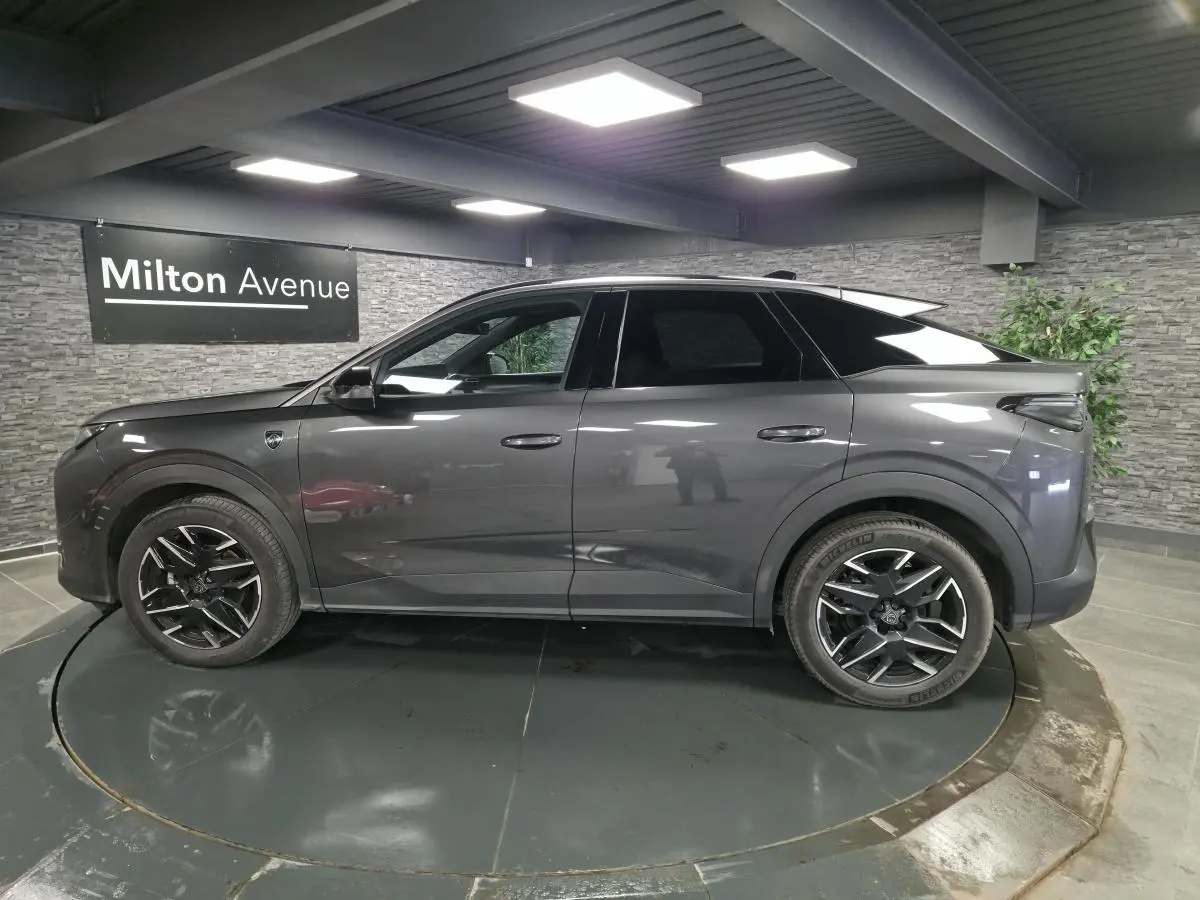 Profil côté gauche du Peugeot 3008 gris métallisé 2025 avec jantes alliage noires et toit noir en showroom.