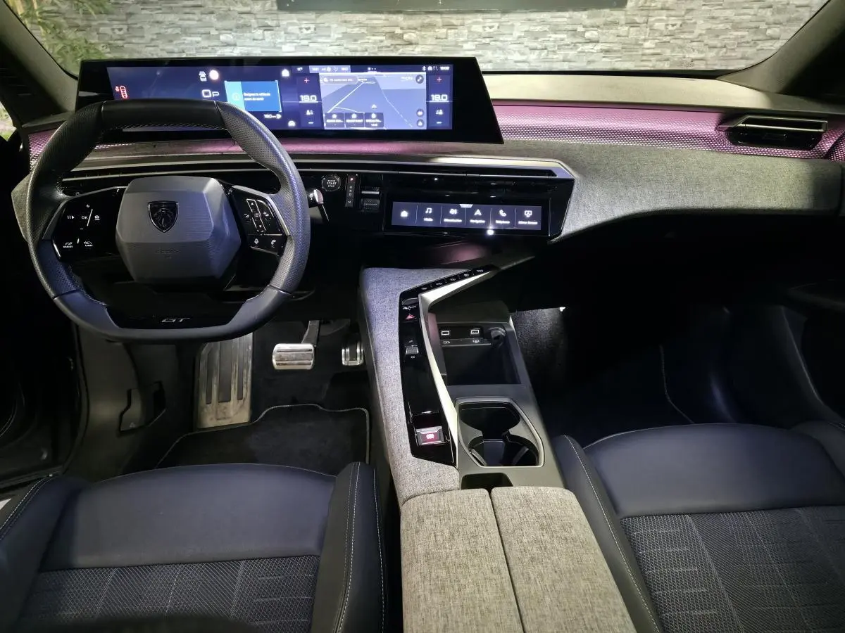 Vue intérieure avant du Peugeot 3008 gris 2025, tableau de bord avec écran panoramique et éclairage d'ambiance violet.