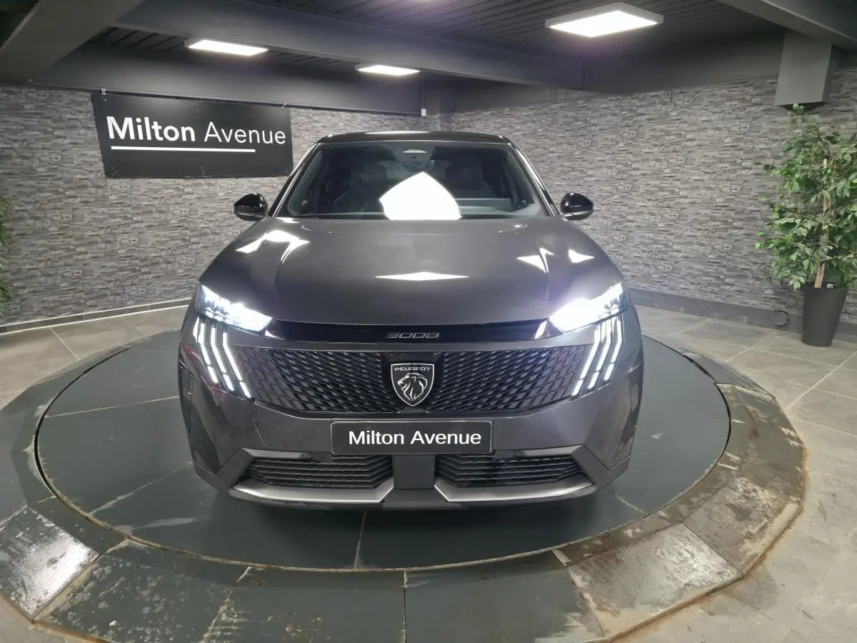 Peugeot 3008 gris vue de face, avec calandre noire et feux LED à griffes allumés dans un showroom.