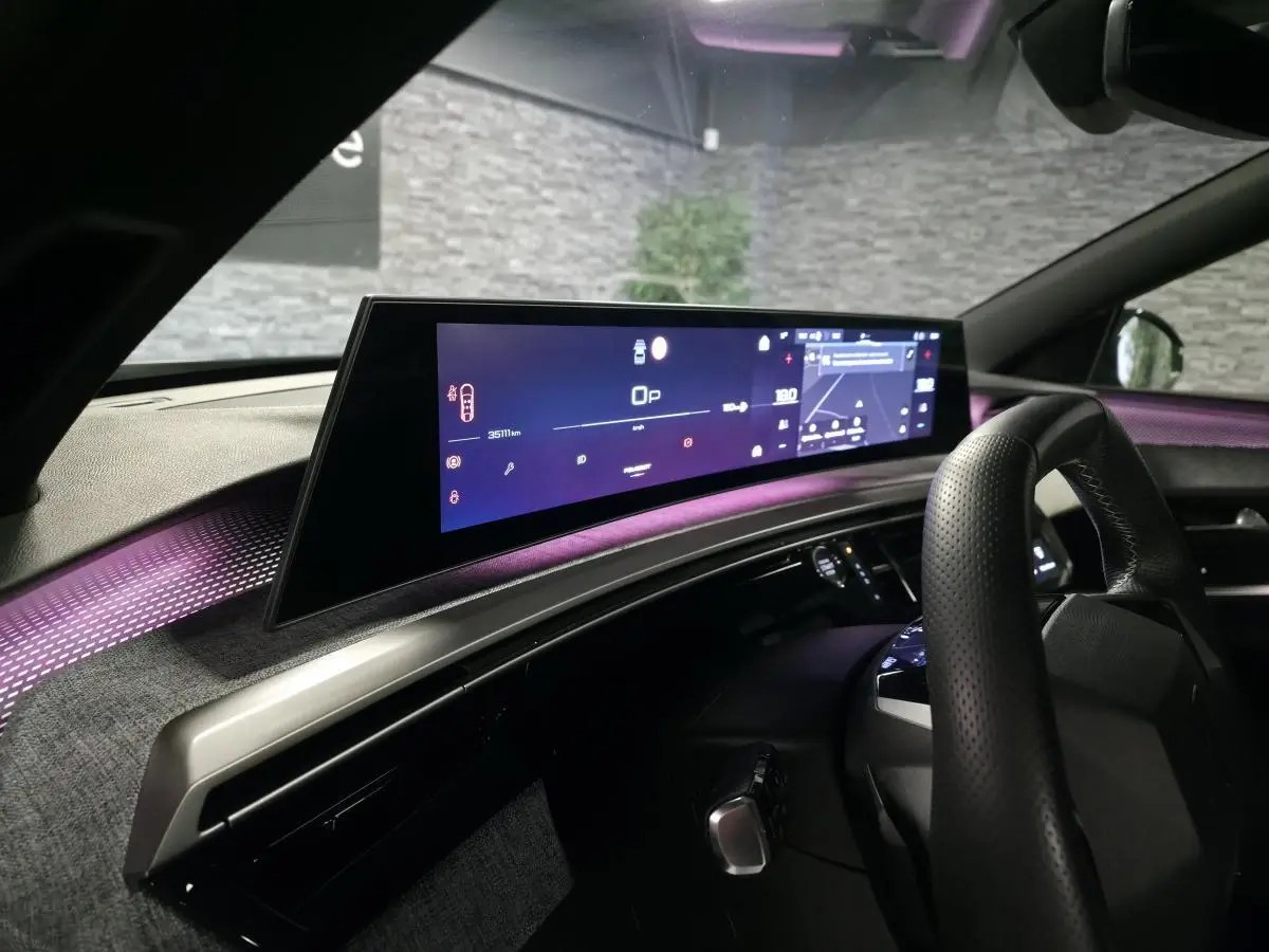 Vue intérieure du tableau de bord du Peugeot 3008 gris 2025 avec écran panoramique et éclairage d'ambiance violet.
