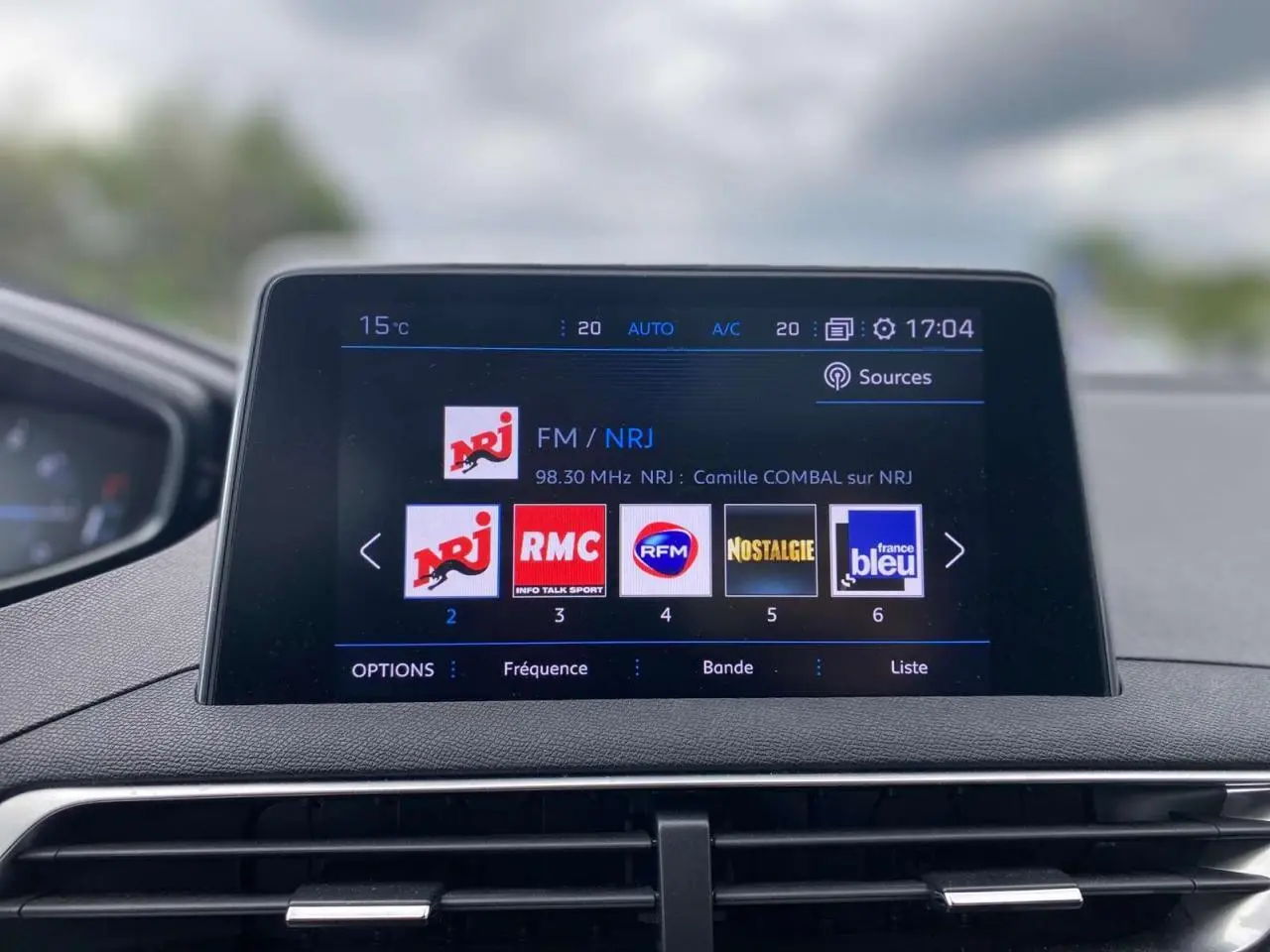 Écran tactile central du Peugeot 3008 blanc 2019 affichant les stations radio avec tableau de bord en arrière-plan flou.