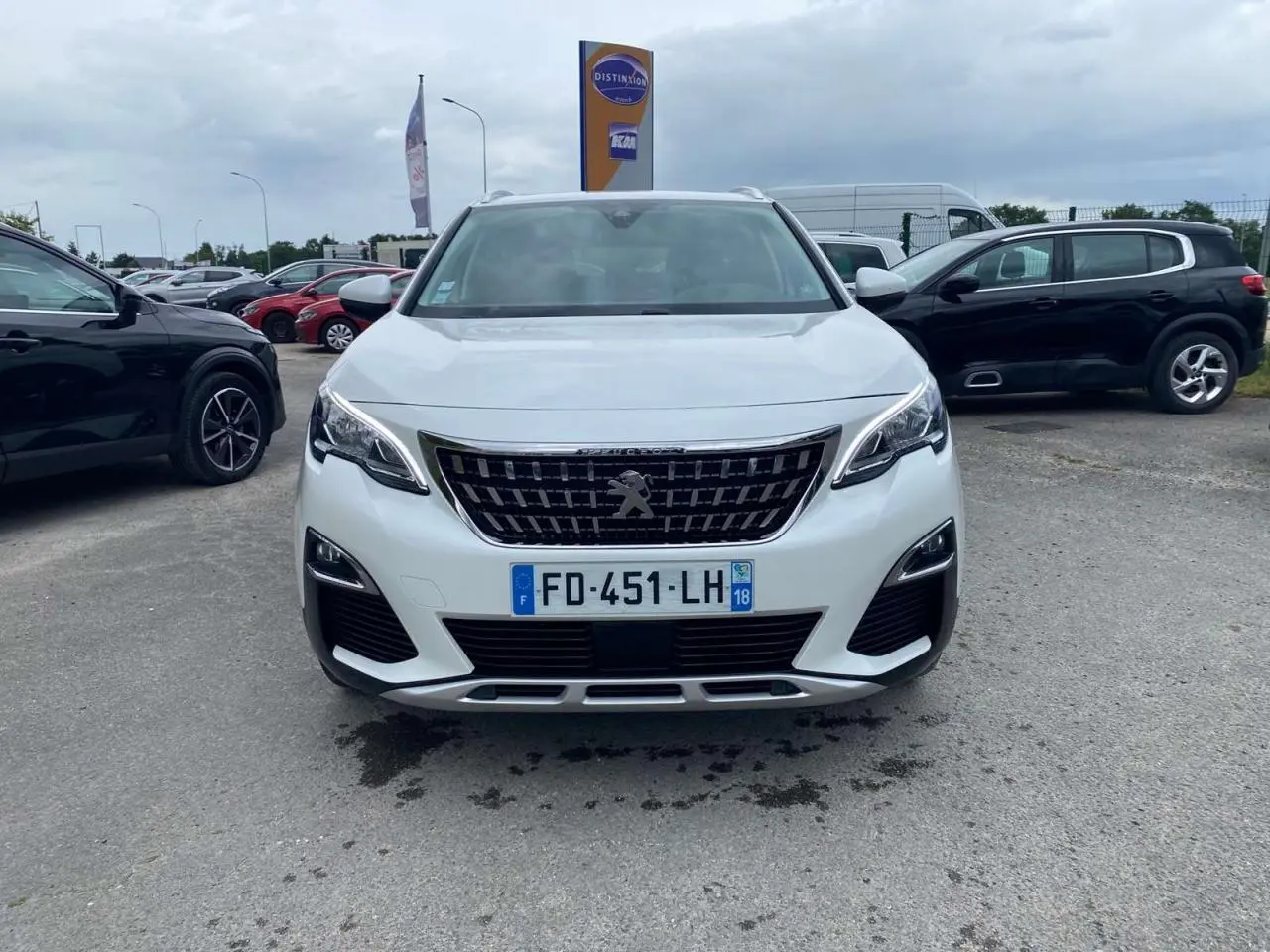 Vue avant d'un Peugeot 3008 blanc nacré avec calandre noire et barres de toit en aluminium sous un ciel nuageux.