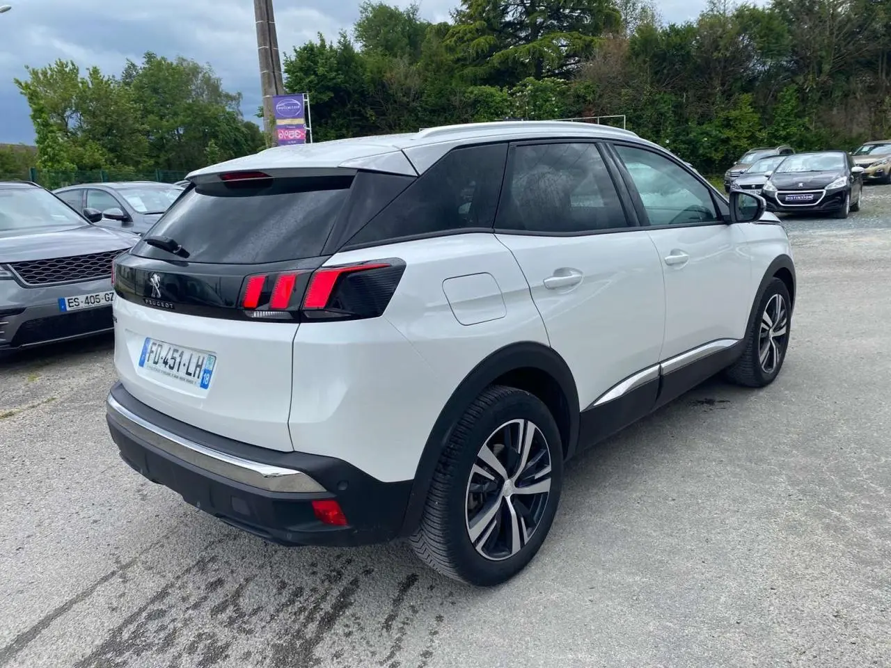 Vue 3/4 arrière droite d’un Peugeot 3008 blanc nacré avec jantes alliage bi-ton et barres de toit profilées en aluminium.