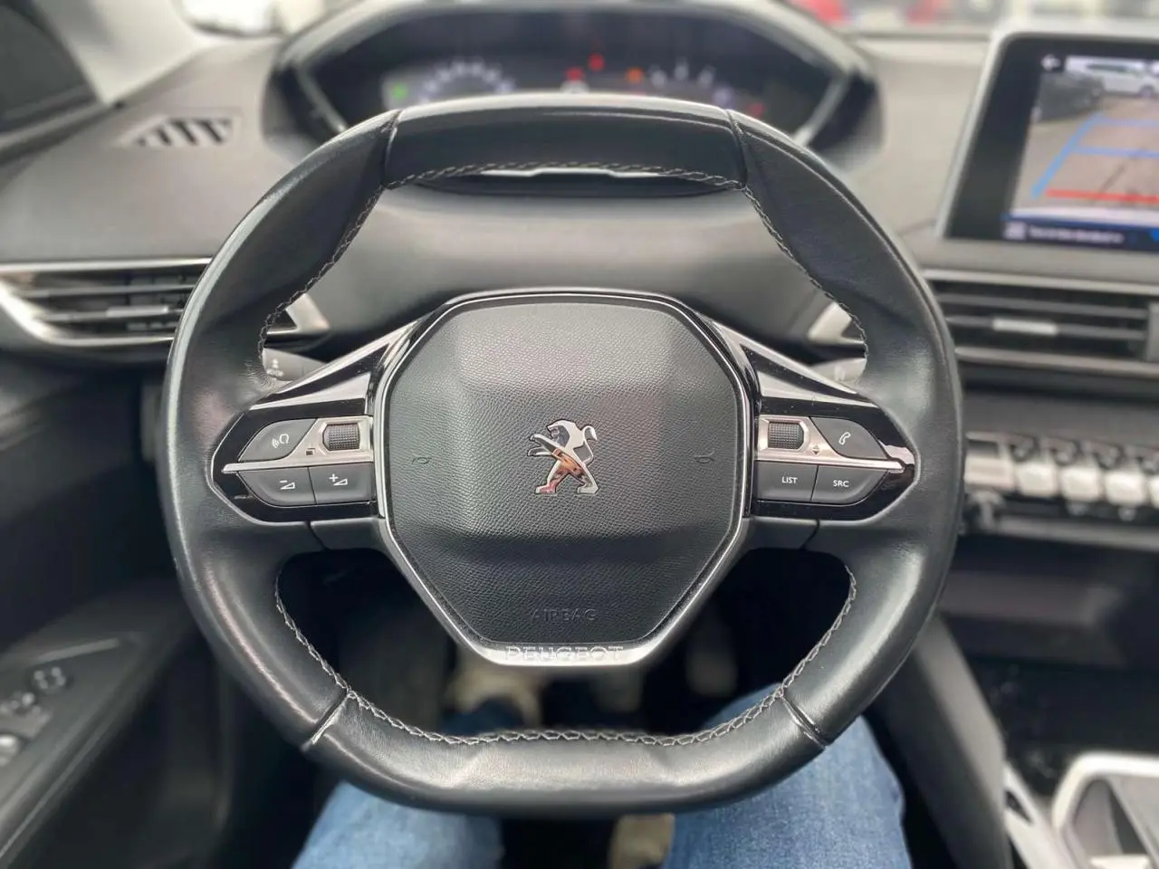 Vue rapprochée du volant compact noir du Peugeot 3008 2019 avec commandes intégrées et tableau de bord flou en arrière-plan.