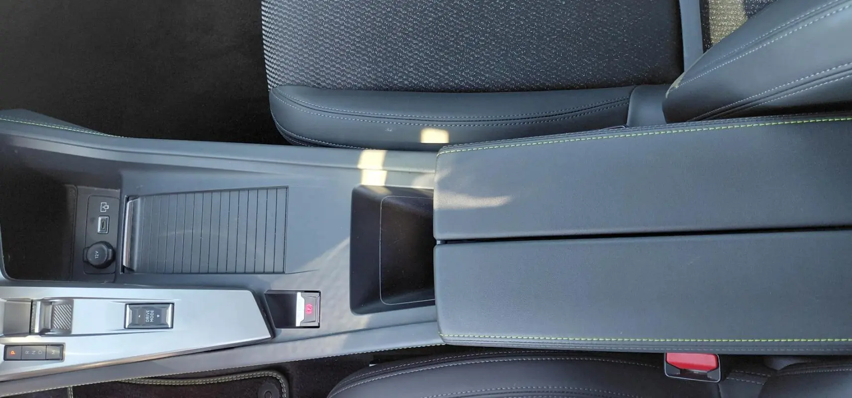 Vue plongeante sur l'accoudoir central gris avec surpiqûres vertes et console centrale de la Peugeot 308 Hybrid 145 e-DCS6 GT.