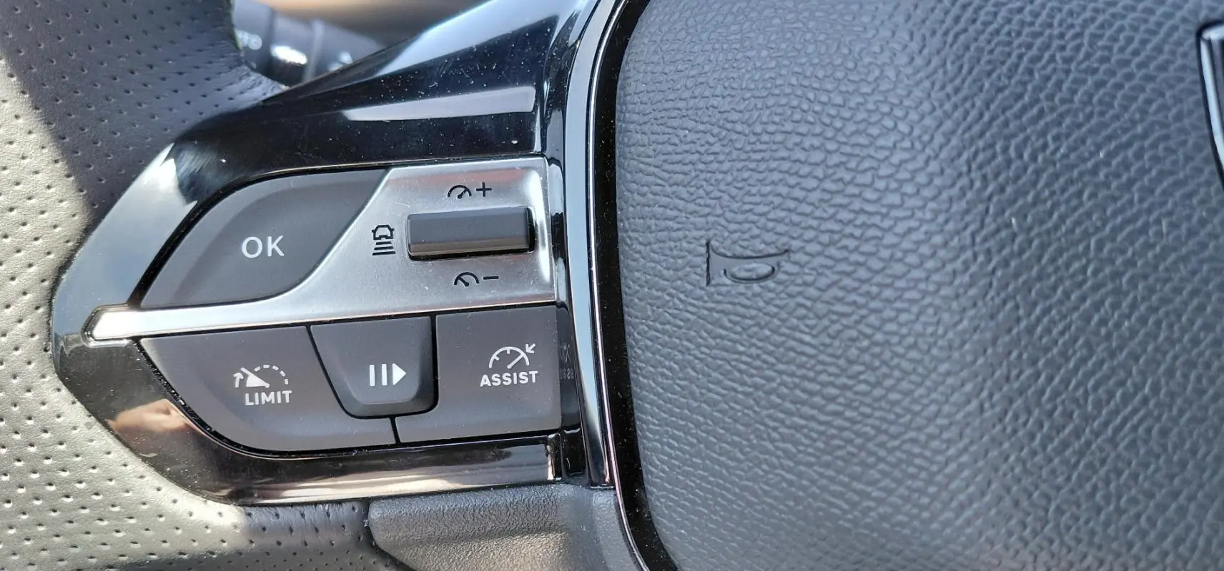Gros plan sur les commandes du volant cuir perforé de la Peugeot 308 Hybrid 145 e-DCS6 GT, boutons régulateur et limiteur.