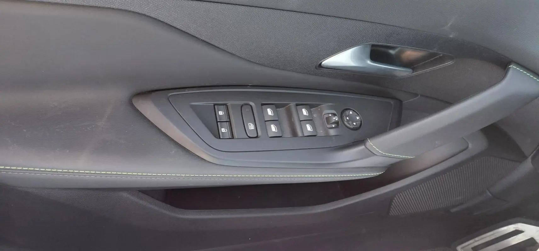 Détail de la porte côté conducteur de la Peugeot 308 Hybrid gris, avec commandes électriques et surpiqûres vertes.