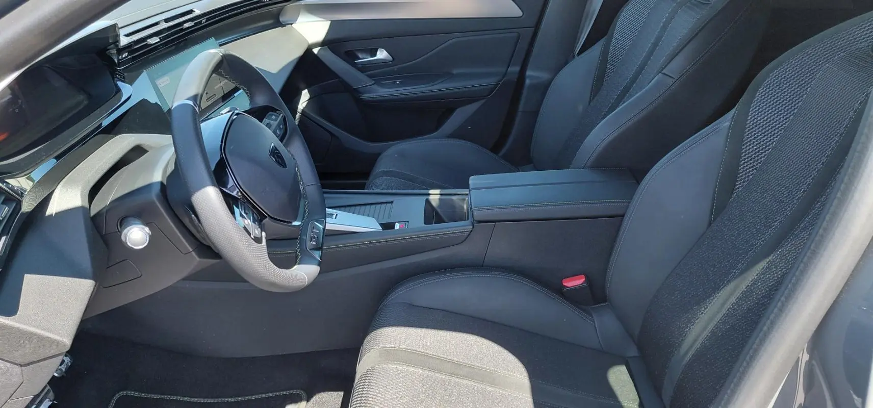 Intérieur avant droit de la Peugeot 308 Hybrid 145 e-DCS6 GT 2025, sièges noirs et volant cuir avec cockpit numérique.
