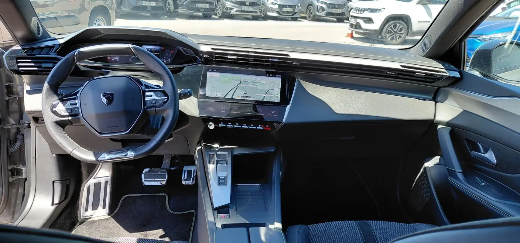Vue intérieure avant du Peugeot 308 Hybrid 145 e-DCS6 GT gris, avec volant cuir et écran tactile central affichant la navigation.