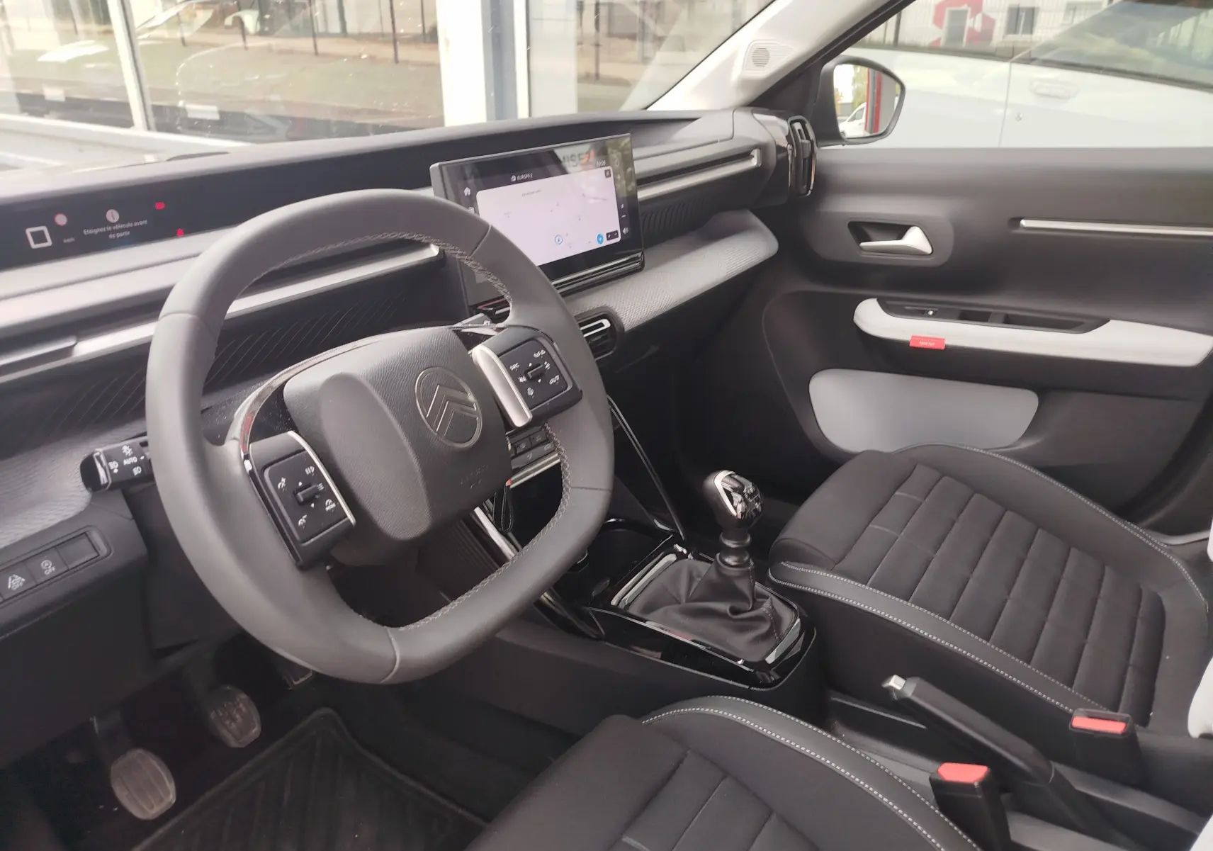 Vue intérieure côté conducteur de la Citroën C3 2025, volant multifonction, écran tactile et sellerie noire avec surpiqûres grises.