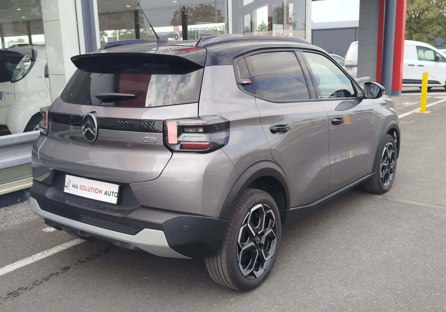 Vue 3/4 arrière droite d'une Citroën C3 gris foncé avec toit noir, jantes bi-ton et feux arrière LED distinctifs.