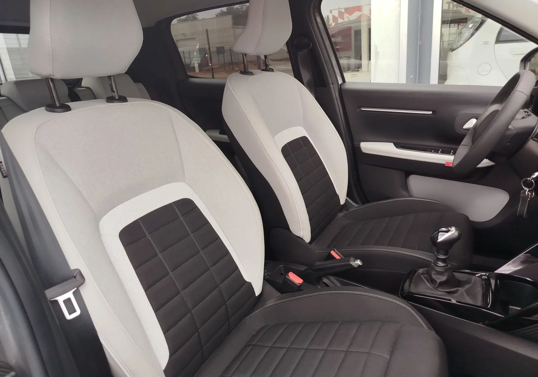 Vue intérieure côté avant droit de la Citroën C3 1.2 Turbo 2025, sièges bicolores gris clair et noir avec boîte manuelle.