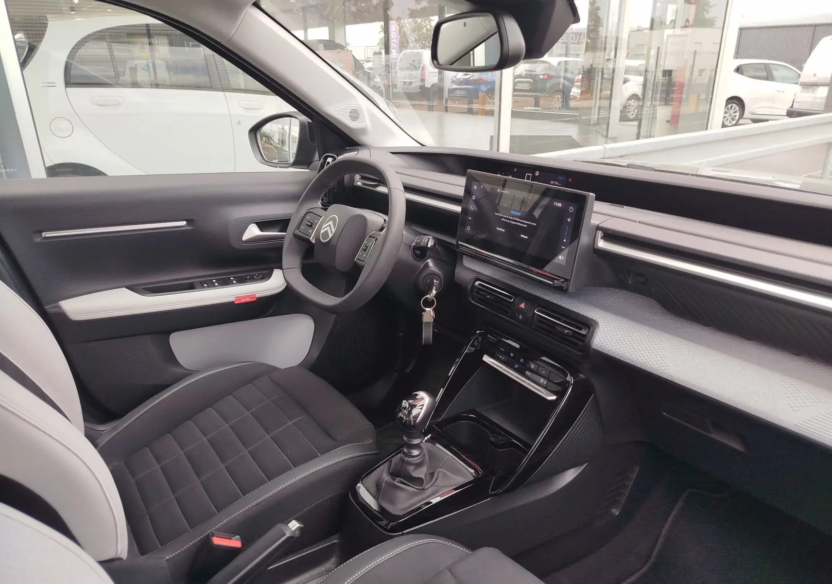 Intérieur avant droit de la Citroën C3 2025 gris foncé, volant multifonction, écran tactile et boîte manuelle visible.