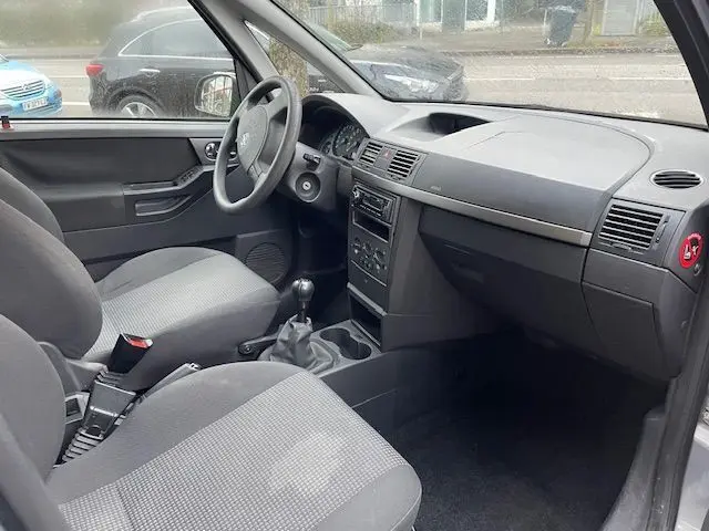 Intérieur avant droit de l'Opel Meriva grise 2010, montrant tableau de bord simple et sièges tissu gris.