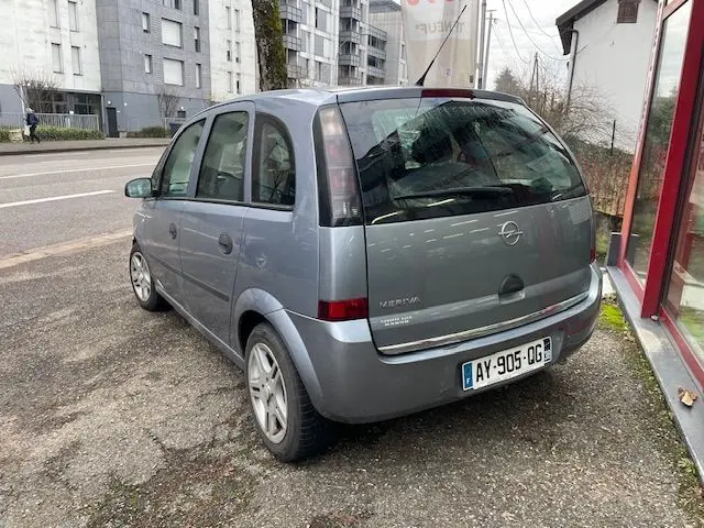 Vue 3/4 arrière droite d'une Opel Meriva grise 2010, compacte et cinq portes, garée près d'un bâtiment en ville.