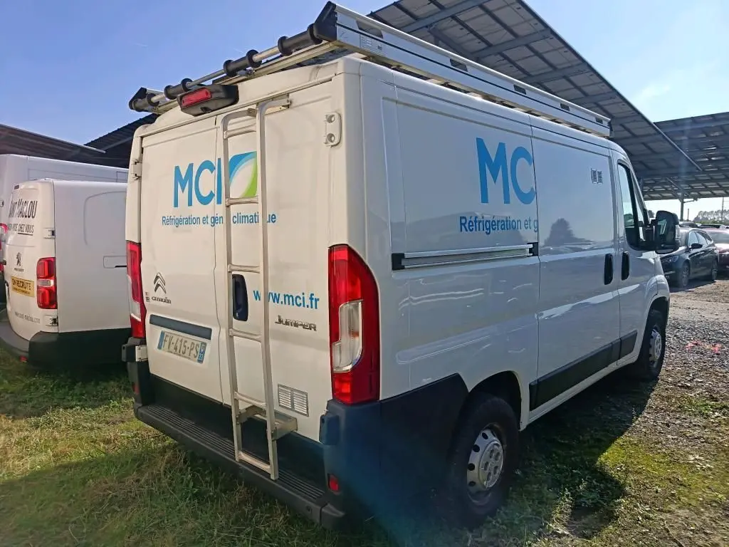 Vue 3/4 arrière droite d'un utilitaire Citroën Jumper blanc avec galerie et marquage publicitaire MCI sur les côtés et portes arrière.