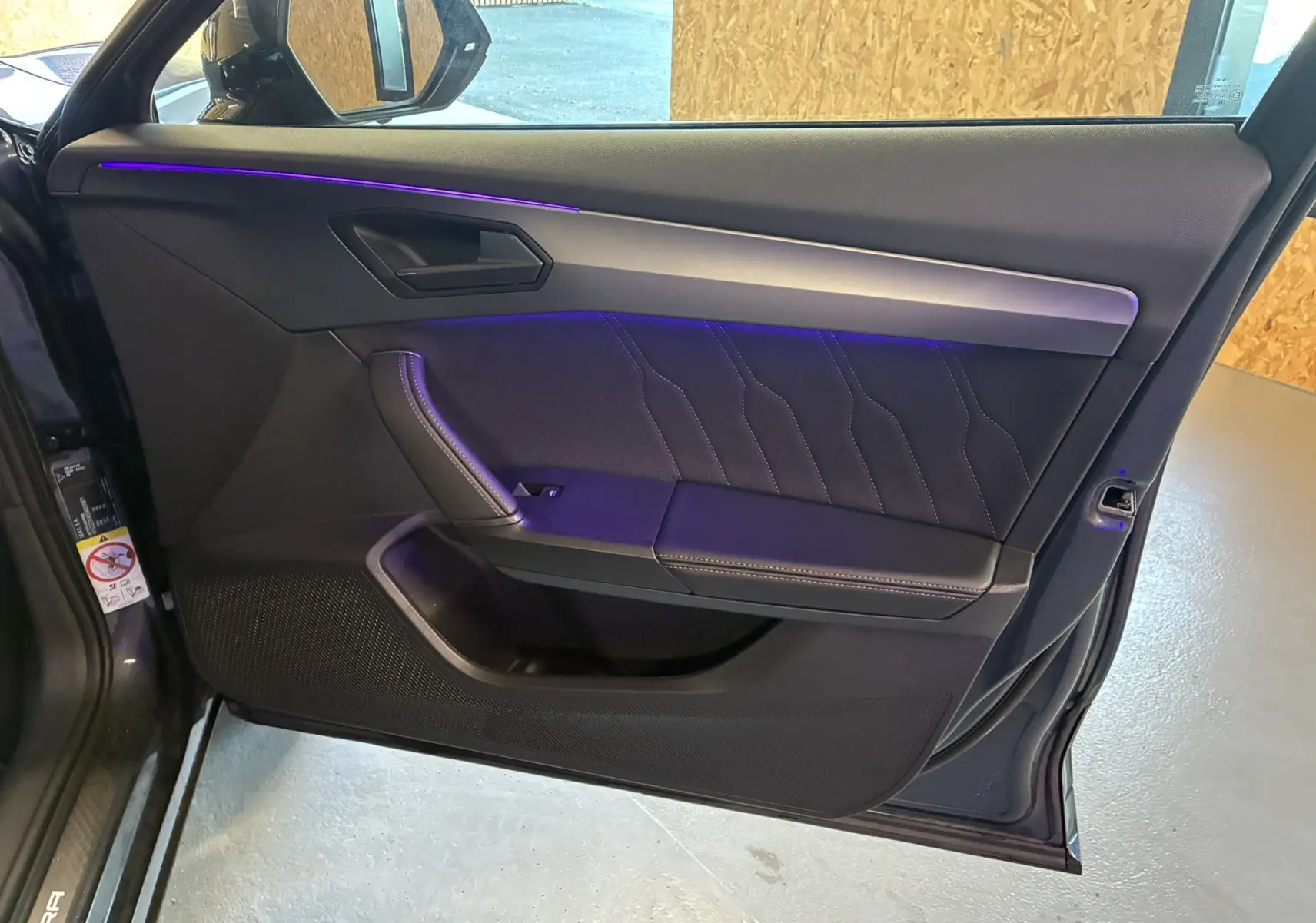 Intérieur côté gauche de la porte avant d'une CUPRA Formentor gris foncé avec éclairage d'ambiance violet et finitions noires.