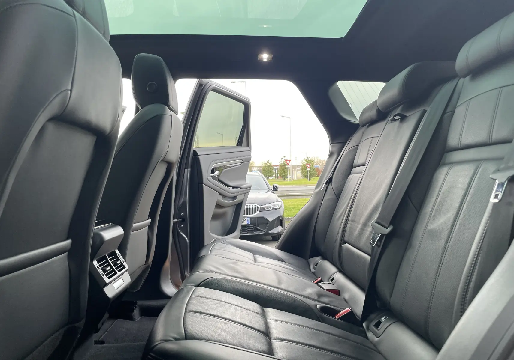 Vue intérieure arrière du Range Rover Evoque 200D SE R-Dynamic en cuir noir, avec porte arrière gauche ouverte et toit panoramique.