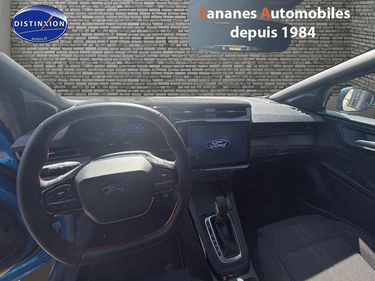 Vue intérieure du poste de conduite du Ford Puma bleu 2025, avec volant sport et écran tactile central allumé.