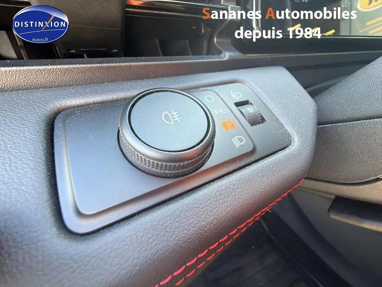 Gros plan sur le bouton de réglage des phares dans l'habitacle du Ford Puma bleu, avec surpiqûres rouges visibles.