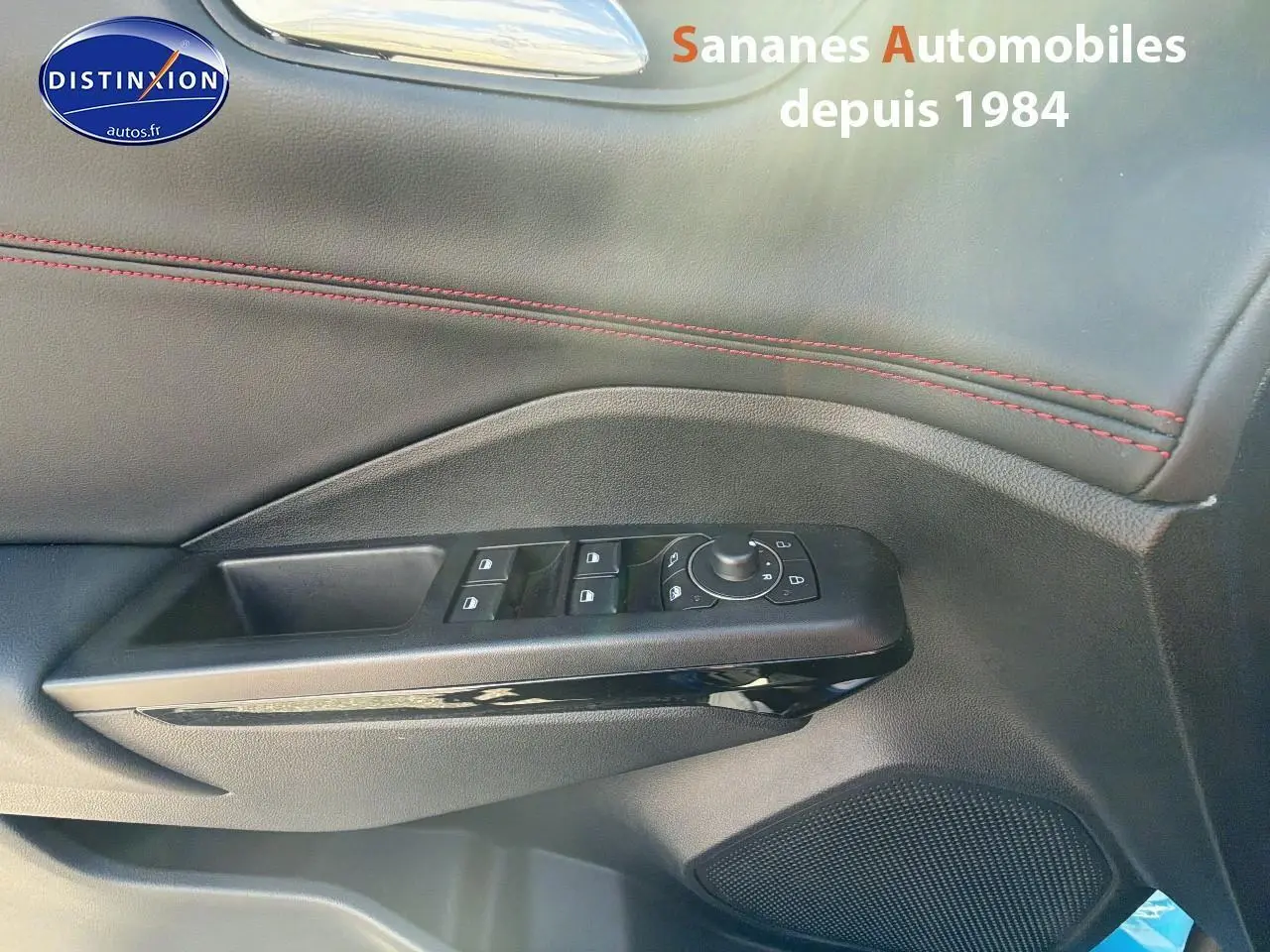 Gros plan sur la porte côté conducteur du Ford Puma bleu, montrant les commandes des vitres et rétroviseurs avec surpiqûres rouges.