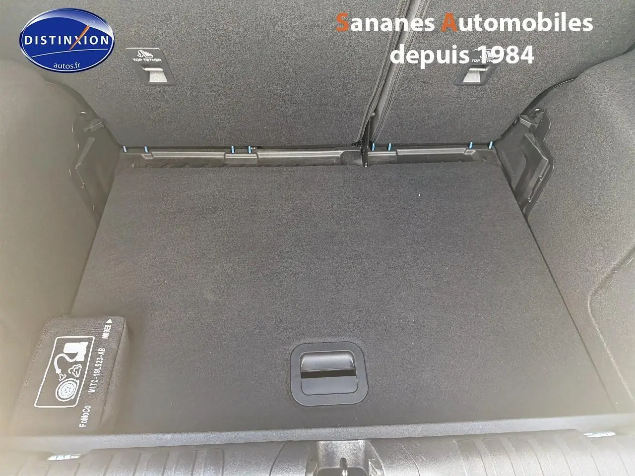 Coffre ouvert d’un Ford Puma bleu, vue de dessus montrant le plancher plat et un kit de réparation pneus rangé sur le côté.