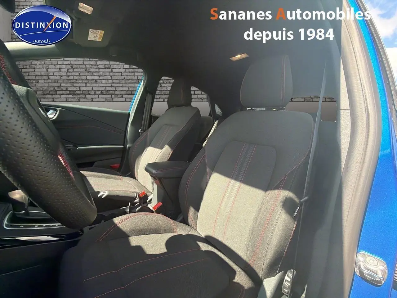 Vue intérieure côté gauche du Ford Puma bleu 2025, sièges tissu avec surpiqûres rouges et volant perforé.