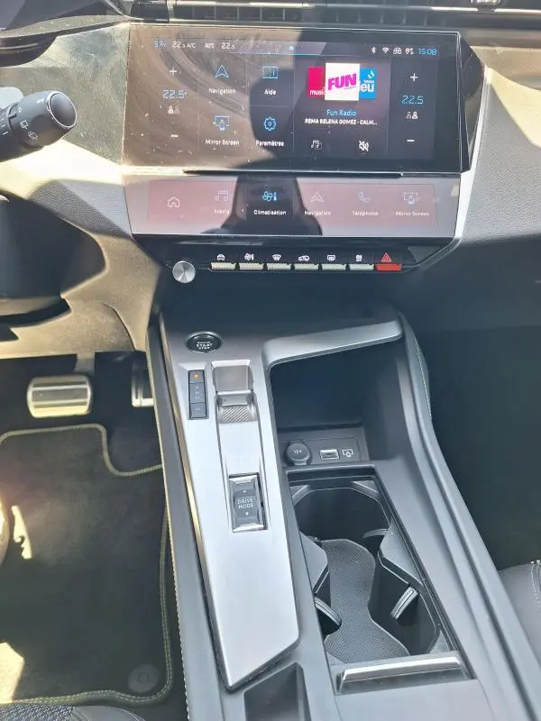 Vue intérieure centrée sur la console centrale et l'écran tactile du Peugeot 308 Hybrid 145 e-DCS6 GT noir de 2025.