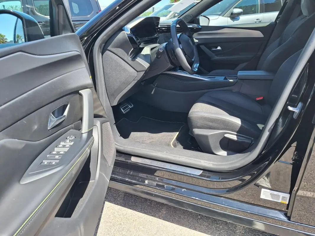 Intérieur côté conducteur de la Peugeot 308 Hybrid 145 GT noir 2025, avec porte ouverte et tableau de bord moderne.
