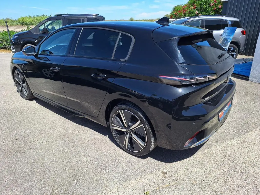 Vue 3/4 arrière droite d'une Peugeot 308 Hybrid 145 e-DCS6 GT noire avec jantes alliage 18 pouces et vitres teintées.
