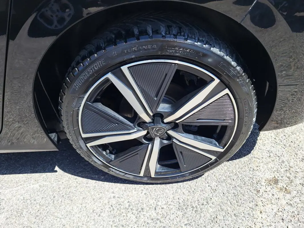 Gros plan sur la jante alliage 18 pouces noire et argentée d'une Peugeot 308 Hybrid 145 e-DCS6 GT noire.