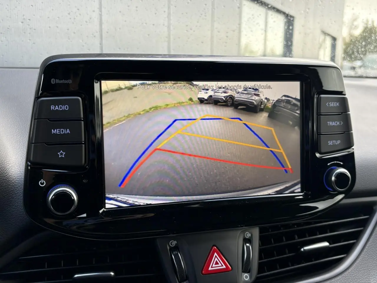 Écran tactile central affichant la caméra de recul avec lignes de guidage dans une Hyundai i30 SW T-GDI 120 Modern gris argent.