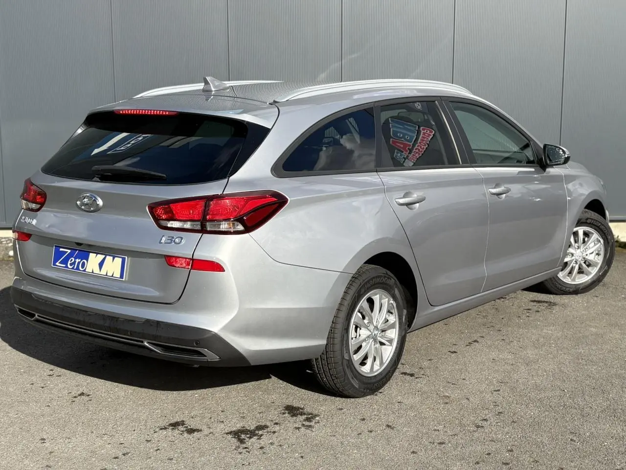 Vue 3/4 arrière droite d'une Hyundai i30 SW T-GDI 120 Modern gris argent métallisé avec jantes alliage et vitres arrière surteintées.
