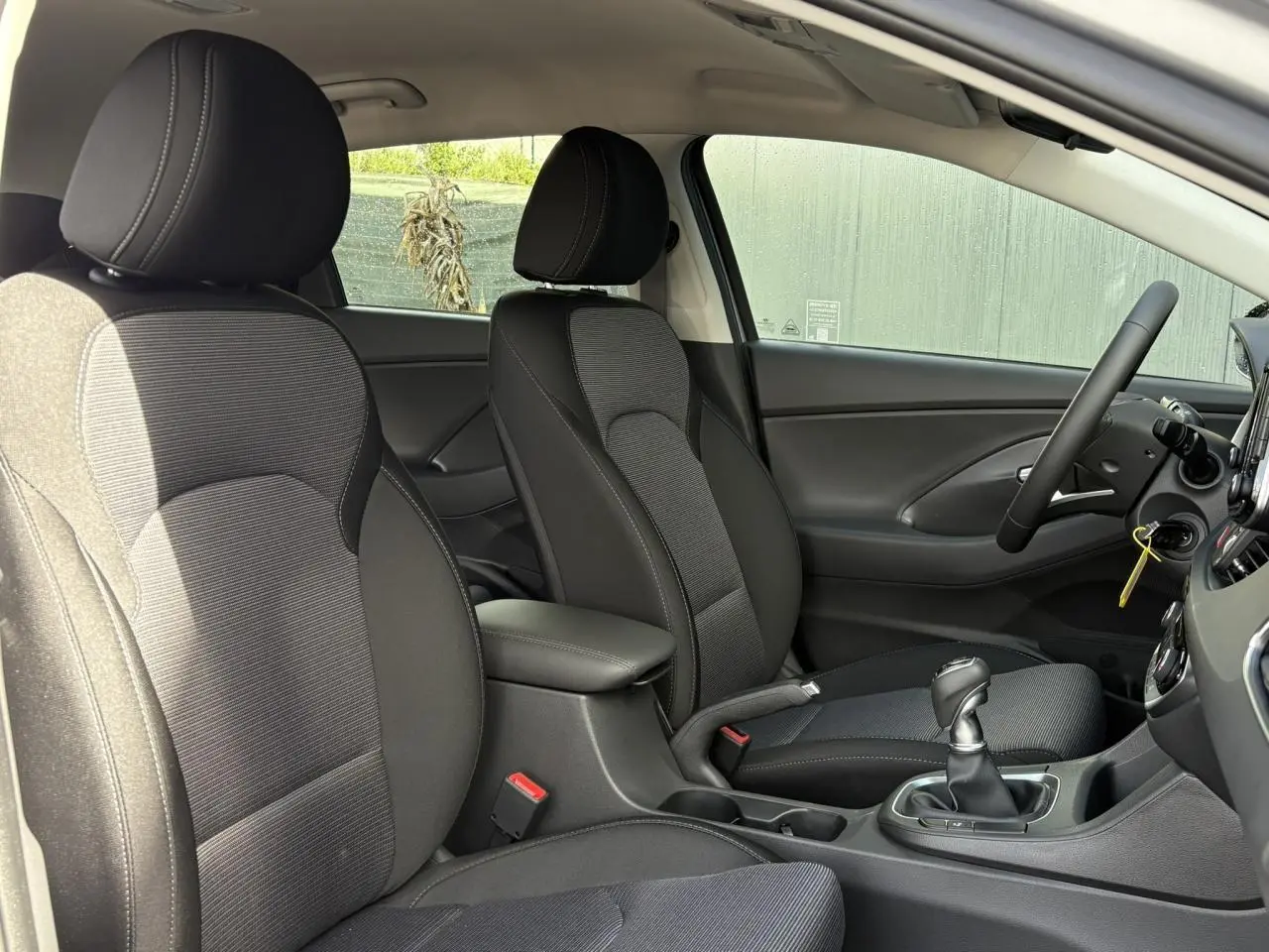 Intérieur de la Hyundai i30 SW T-GDI 120 Modern 2025 vu côté droit, sièges tissu noir et console centrale avec levier manuel.