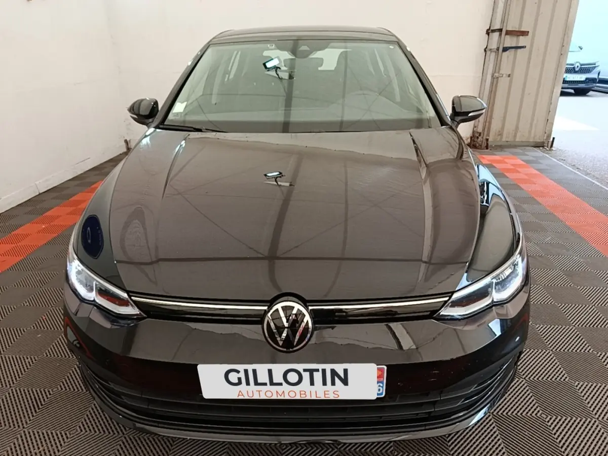 Vue frontale d'une Volkswagen Golf noire 2023 avec phares LED et calandre chromée dans un garage.