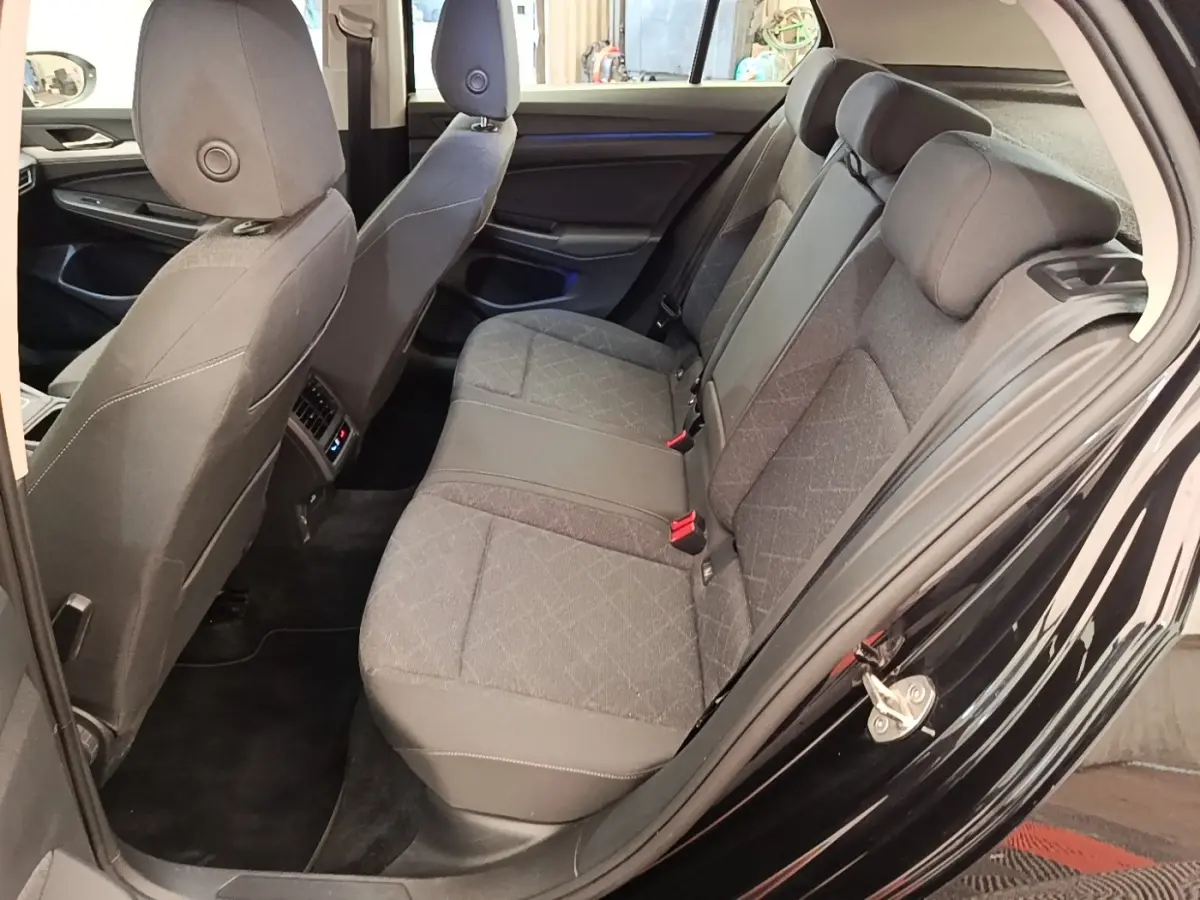 Vue côté gauche arrière de l’habitacle d’une Volkswagen Golf noire 2023, montrant la banquette tissu et les sièges avant.