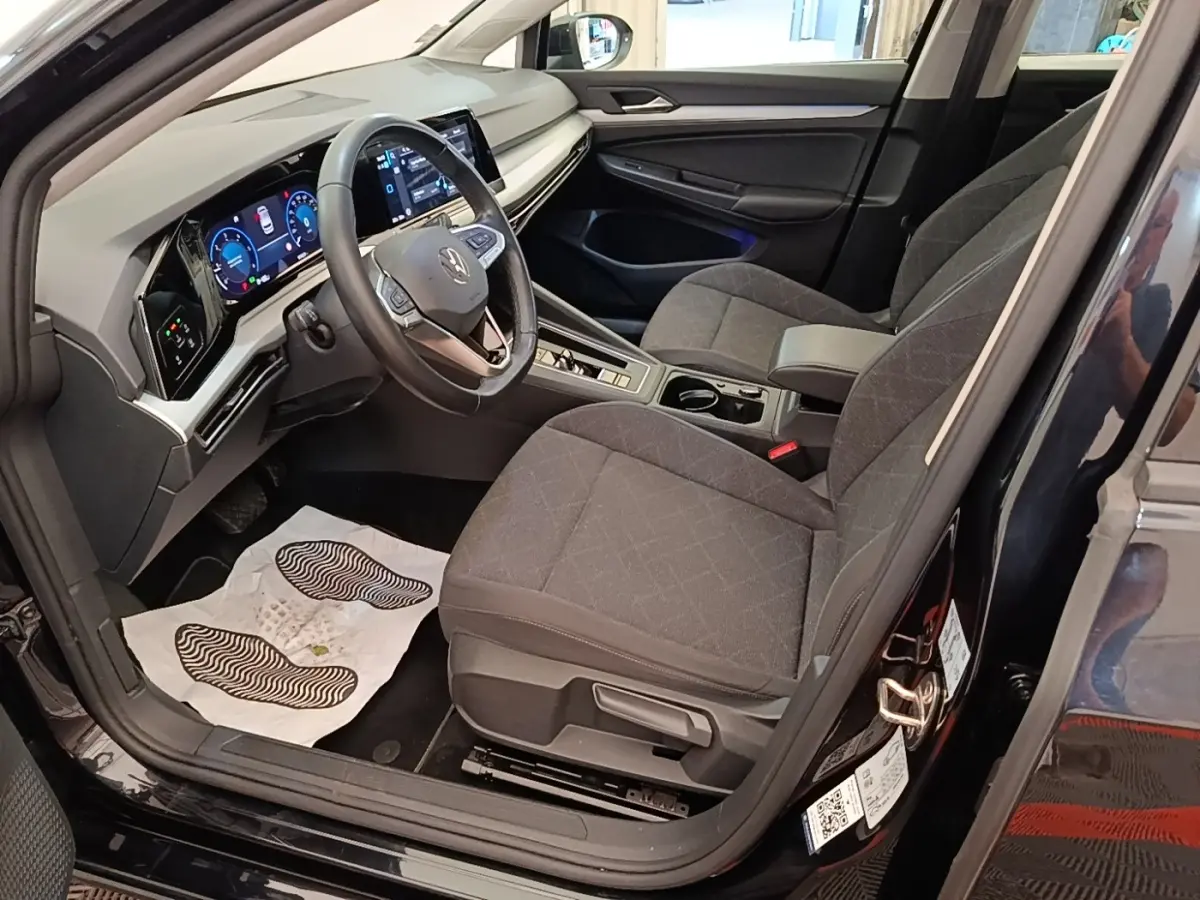 Vue intérieure côté conducteur de la Volkswagen Golf noire 2023, avec tableau de bord digital et sièges tissu gris.