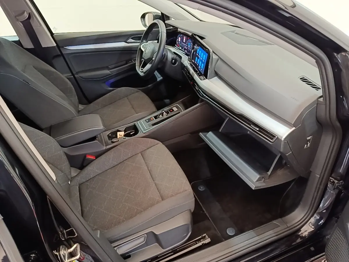 Vue intérieure côté passager de la Volkswagen Golf noire 2023, tableau de bord numérique et boîte à gants ouverte.