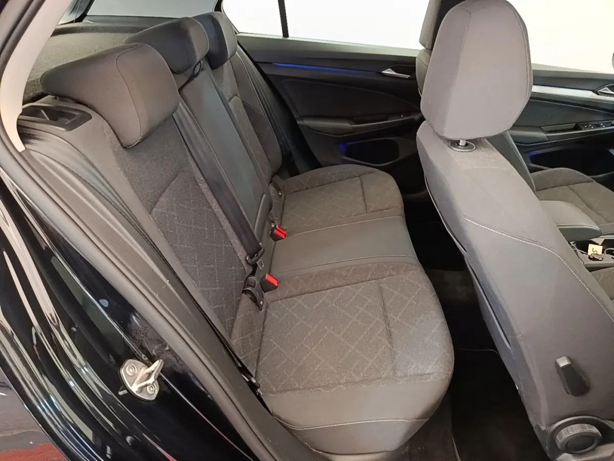 Vue intérieure côté gauche montrant la banquette arrière grise et les sièges avant d'une Volkswagen Golf noire 2023.