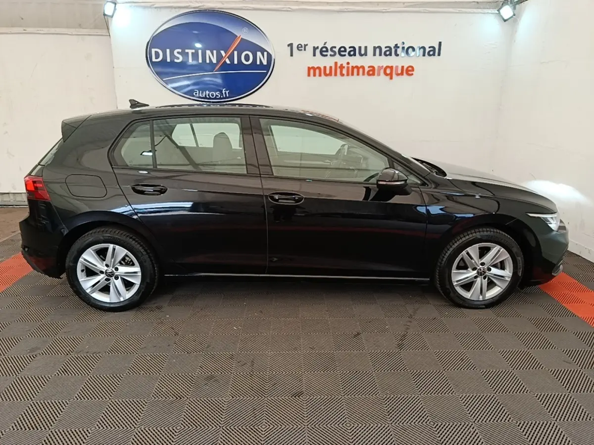 Profil droit d'une Volkswagen Golf noire 2023 garée en intérieur avec jantes alliage et vitres teintées.