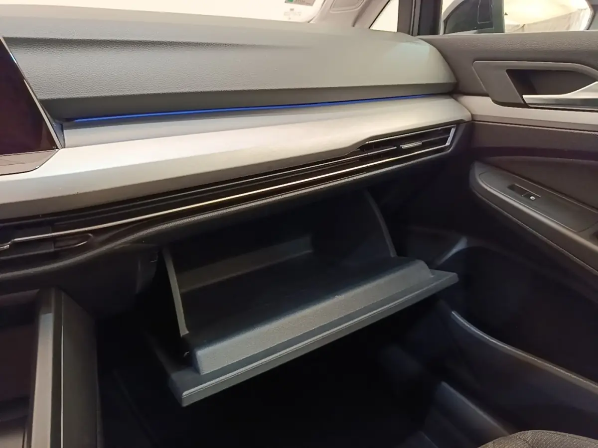 Intérieur de la Volkswagen Golf 2.0 TDI 2023, vue côté passager sur la boîte à gants ouverte et tableau de bord noir avec éclairage bleu.