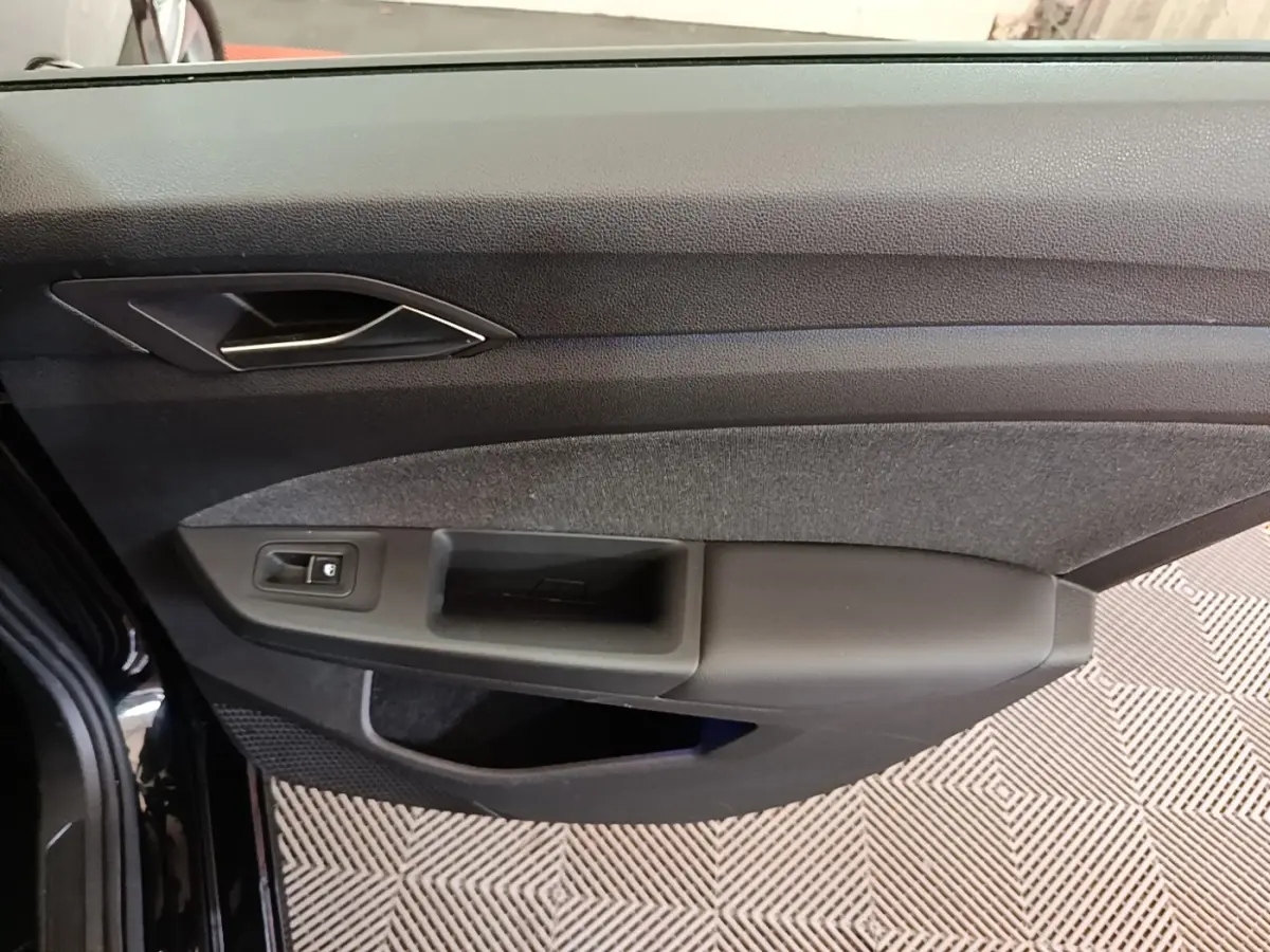 Vue rapprochée de la porte avant gauche noire de la Volkswagen Golf 2023, avec poignée et commande de vitre.