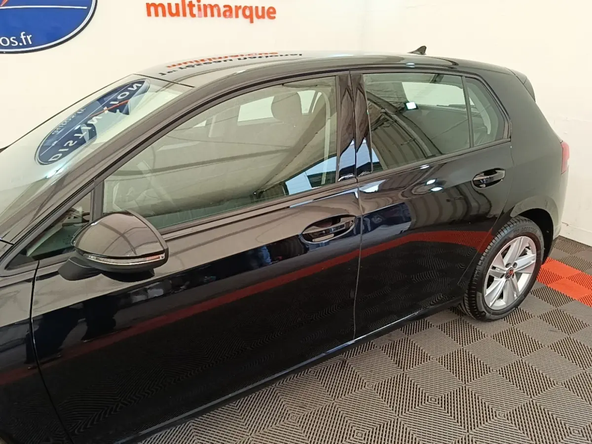 Profil côté gauche d'une Volkswagen Golf noire 2023, avec rétroviseur et jante alliage visibles sur sol intérieur.