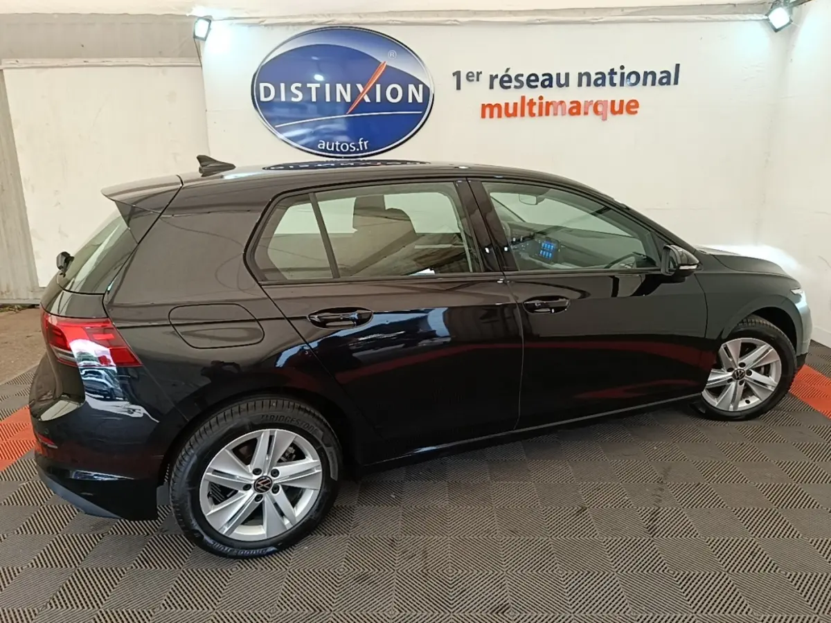 Profil droit d'une Volkswagen Golf noire 2023 dans un showroom avec jantes alliage et vitres teintées.