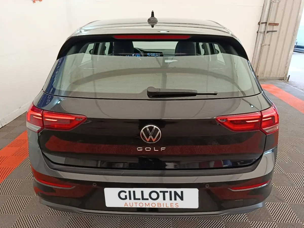 Vue arrière d'une Volkswagen Golf noire 2023 avec feux LED et logo central visible en intérieur showroom.
