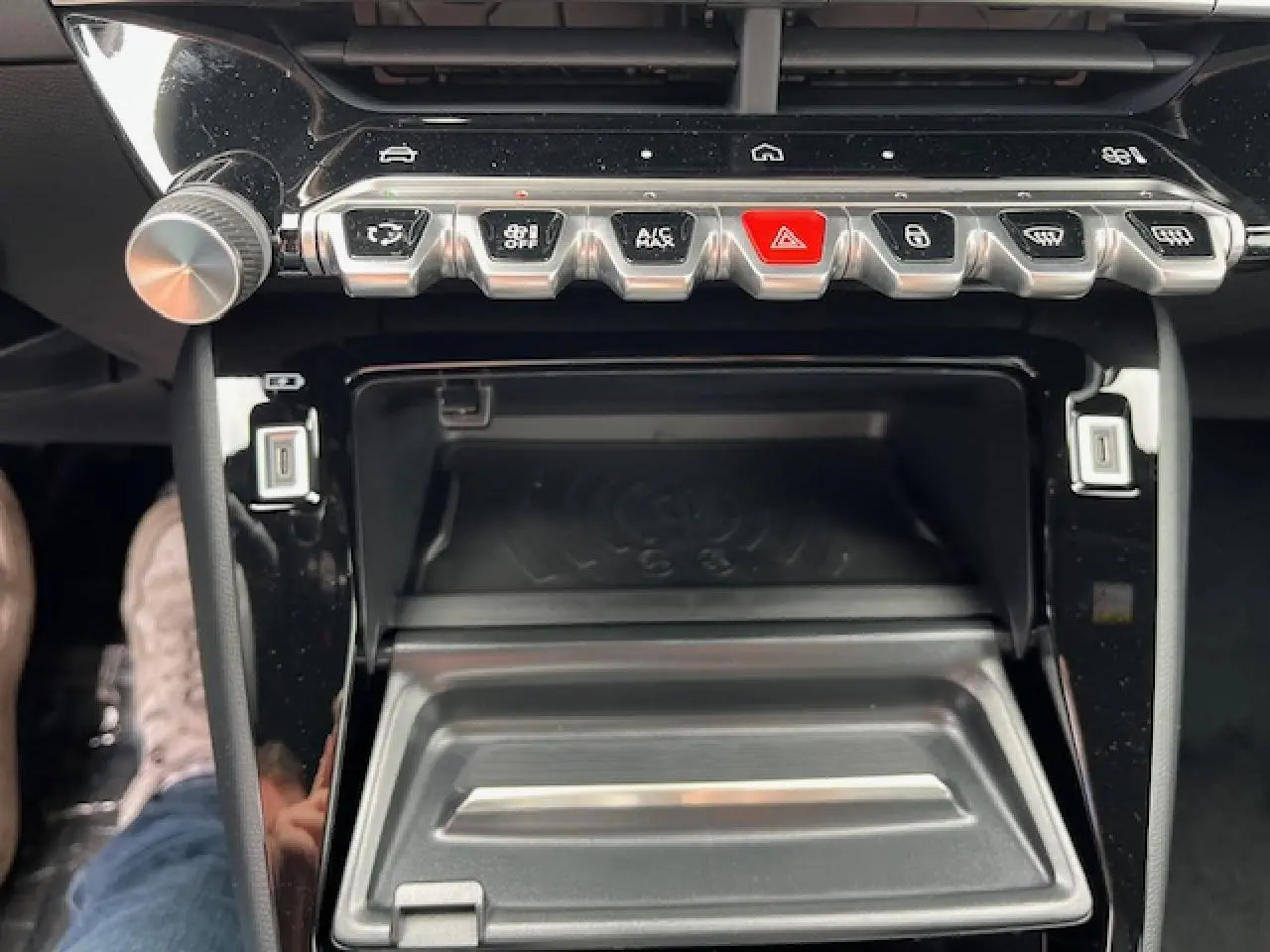 Gros plan sur la console centrale du Peugeot 2008 2026, montrant les boutons de commande et le chargeur smartphone à induction.