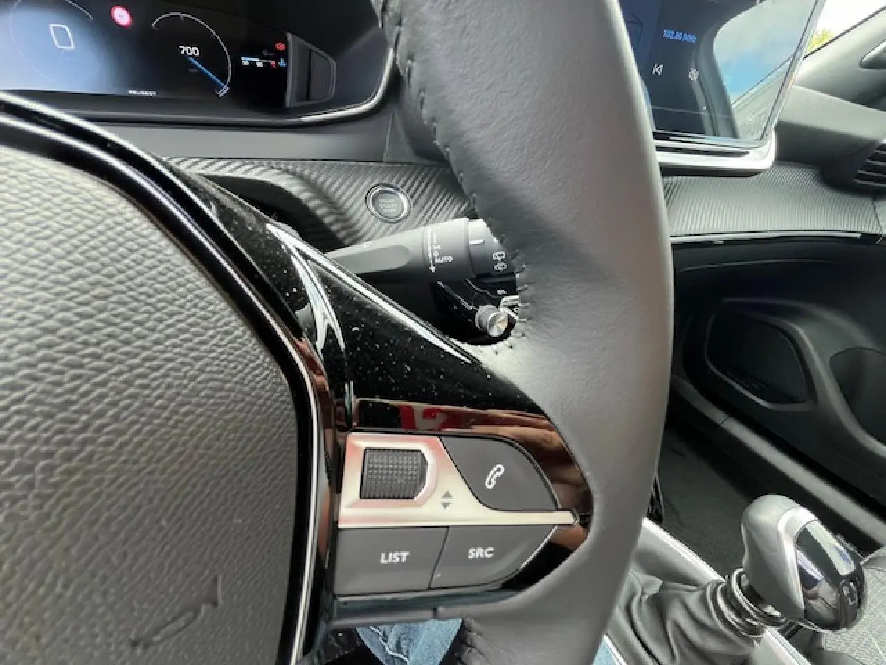 Vue rapprochée du volant et levier de vitesse manuel du Peugeot 2008 blanc, avec commandes audio intégrées et tableau de bord numérique.