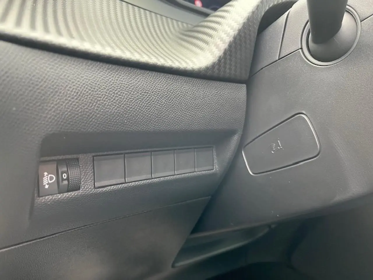 Détail intérieur côté gauche du tableau de bord du Peugeot 2008 2026 avec commandes d’éclairage et texture carbone.