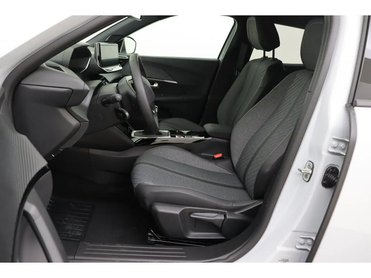 Vue intérieure côté conducteur du Peugeot 2008 blanc Okenite 2026, sièges tissu gris et tableau de bord moderne.
