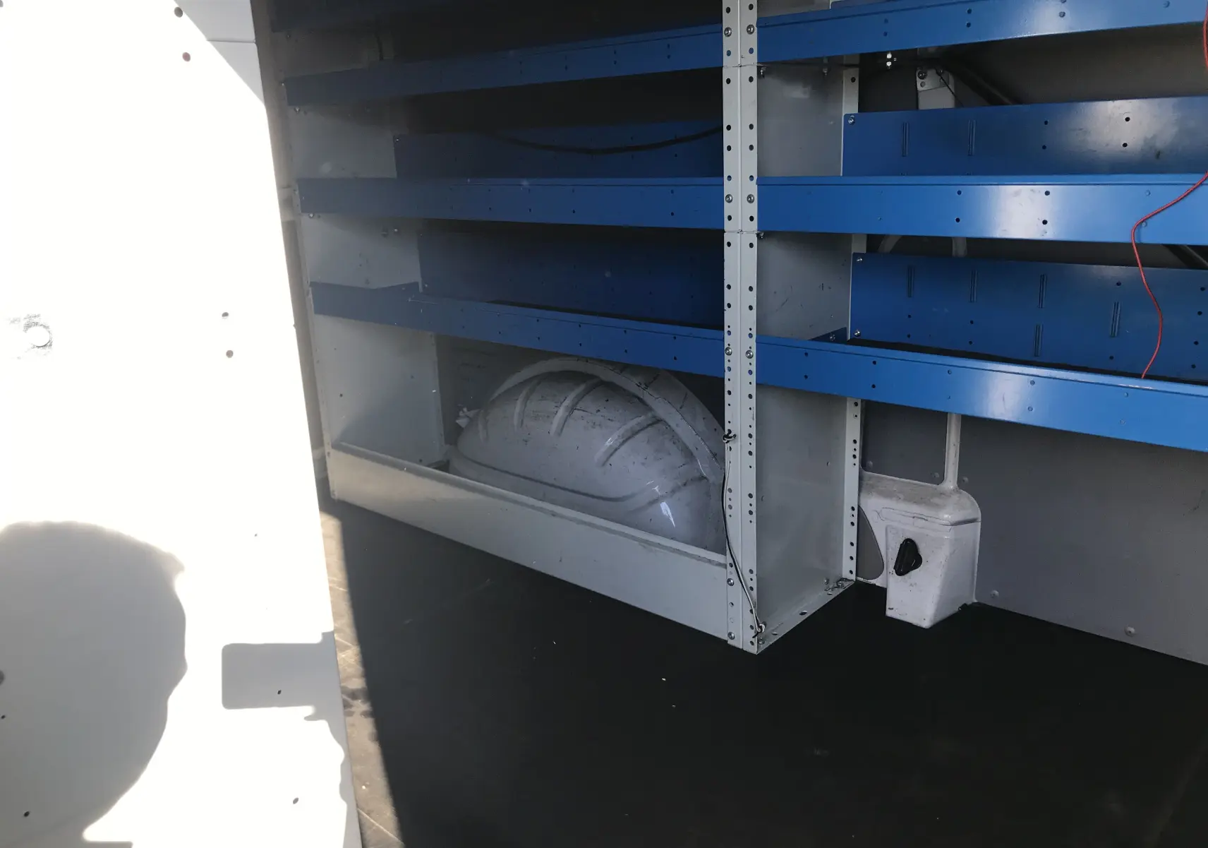 Intérieur du Volkswagen Transporter blanc, vue sur les étagères métalliques bleues et la cloison séparatrice grise.